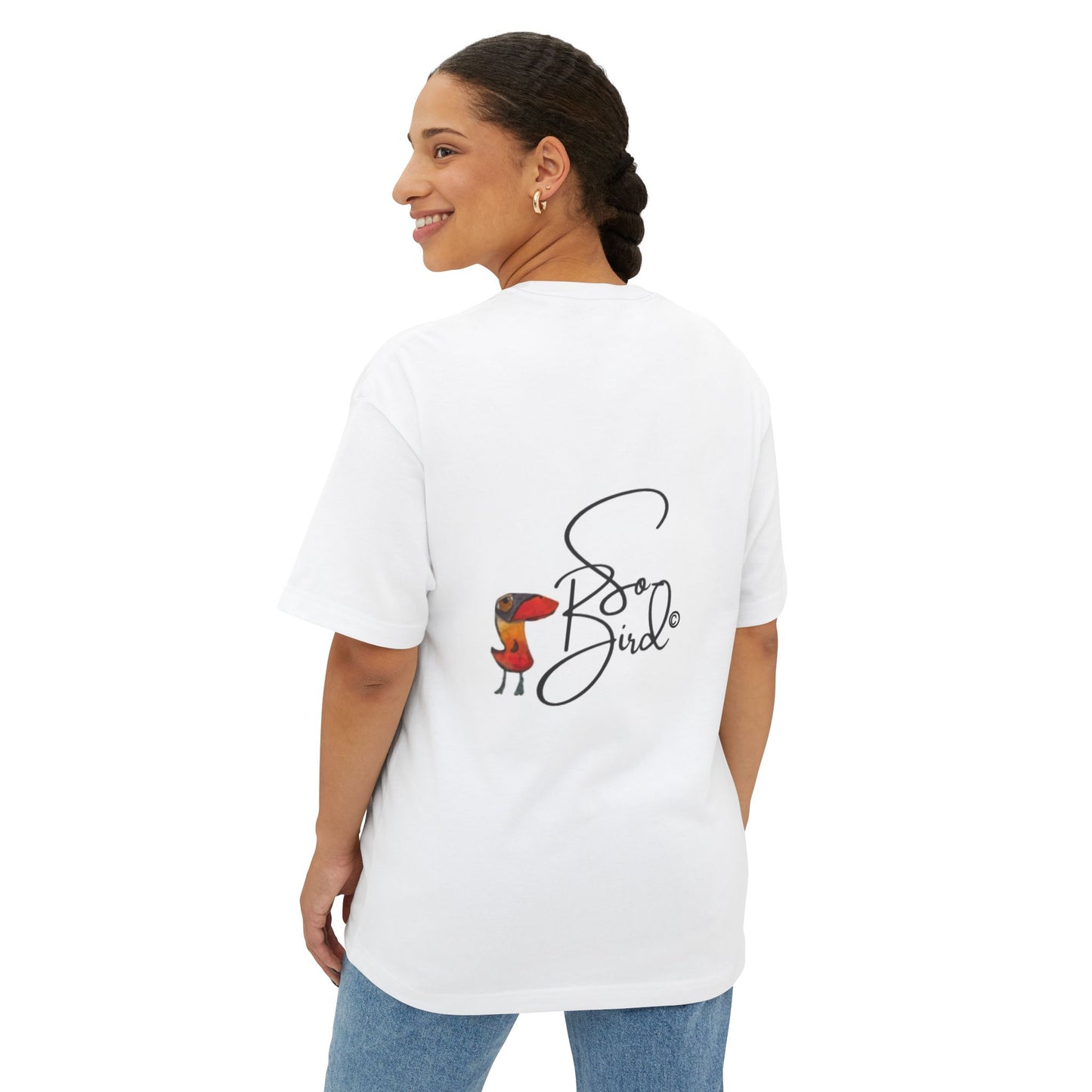 A woman with braided hair smiles over her shoulder, wearing the Printify Recovery Support Unisex Tee—an oversized, relaxed fit featuring a playful small bird in a red jacket and “Sassy Bird” graphic on the back.