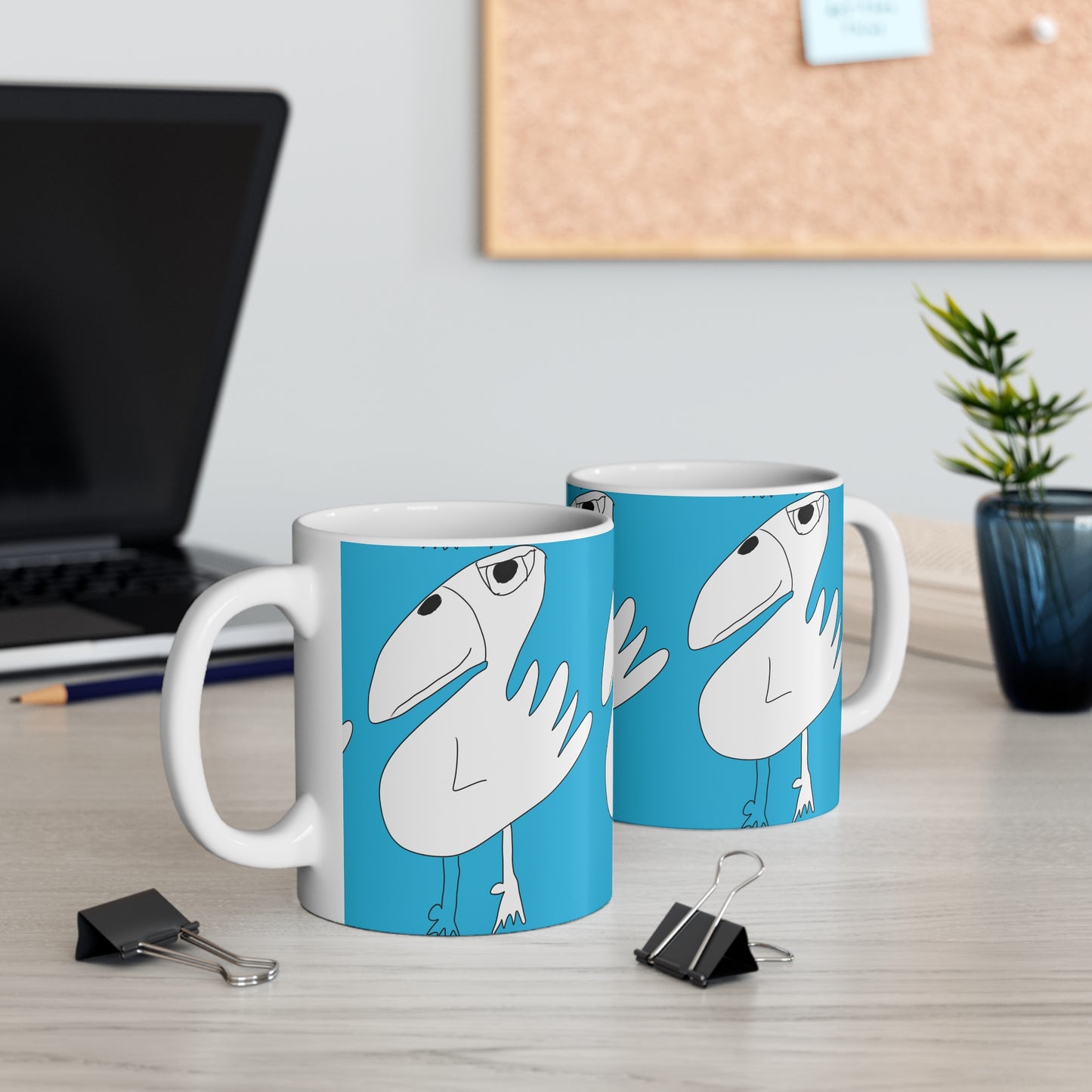 Two Printify 1:1 Mug - 11oz ceramic mugs with a cartoon white bird on blue sit on a desk, making them ideal as sobriety or recovery gifts. Binder clips, a laptop, potted plant, and corkboard complete the scene.