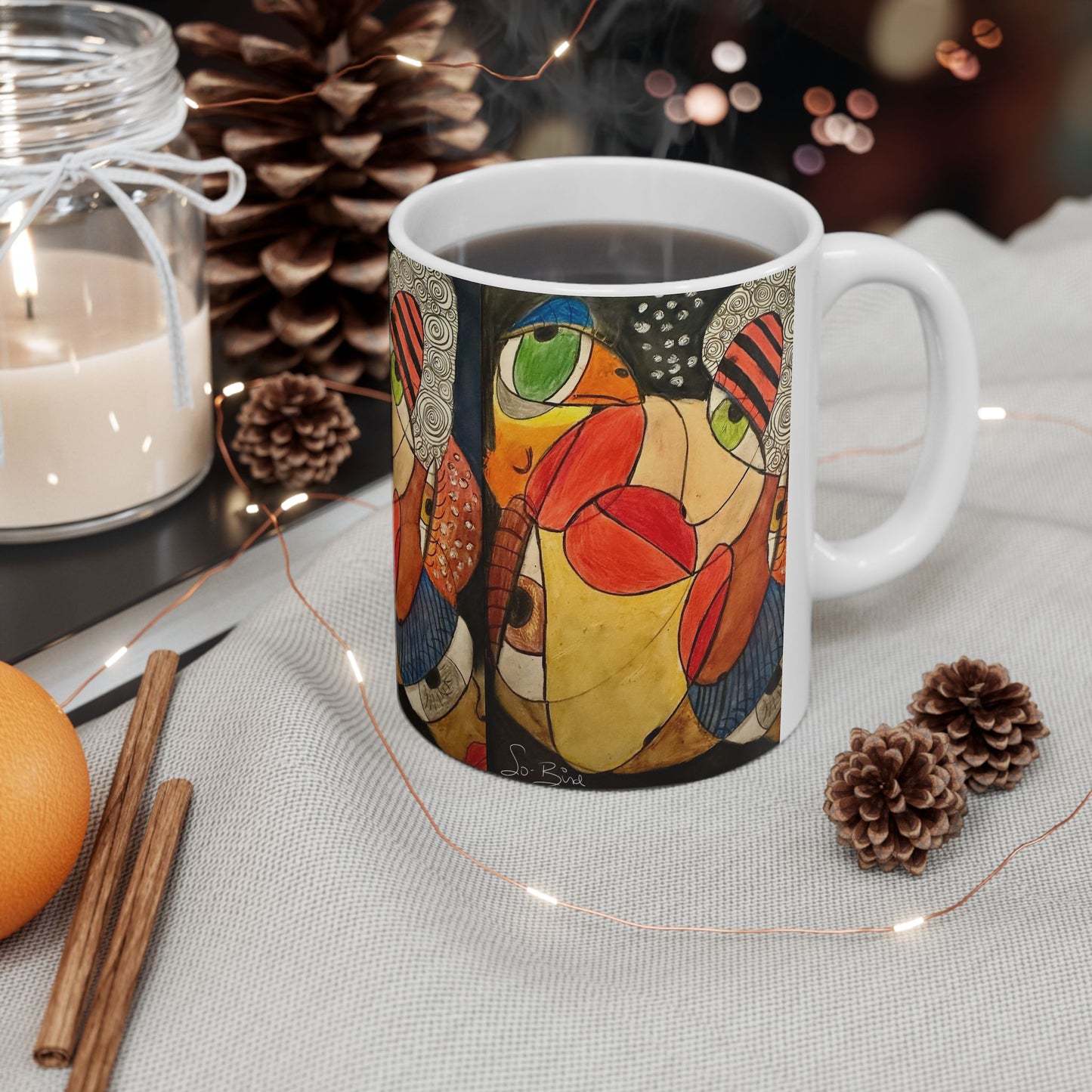 The Printify Ceramic Mug - It's a WE thing Recovery and Sober Gift features a vibrant abstract design, set beside cozy decor like a candle, pinecones, and string lights—perfect for coffee or celebrating sobriety.