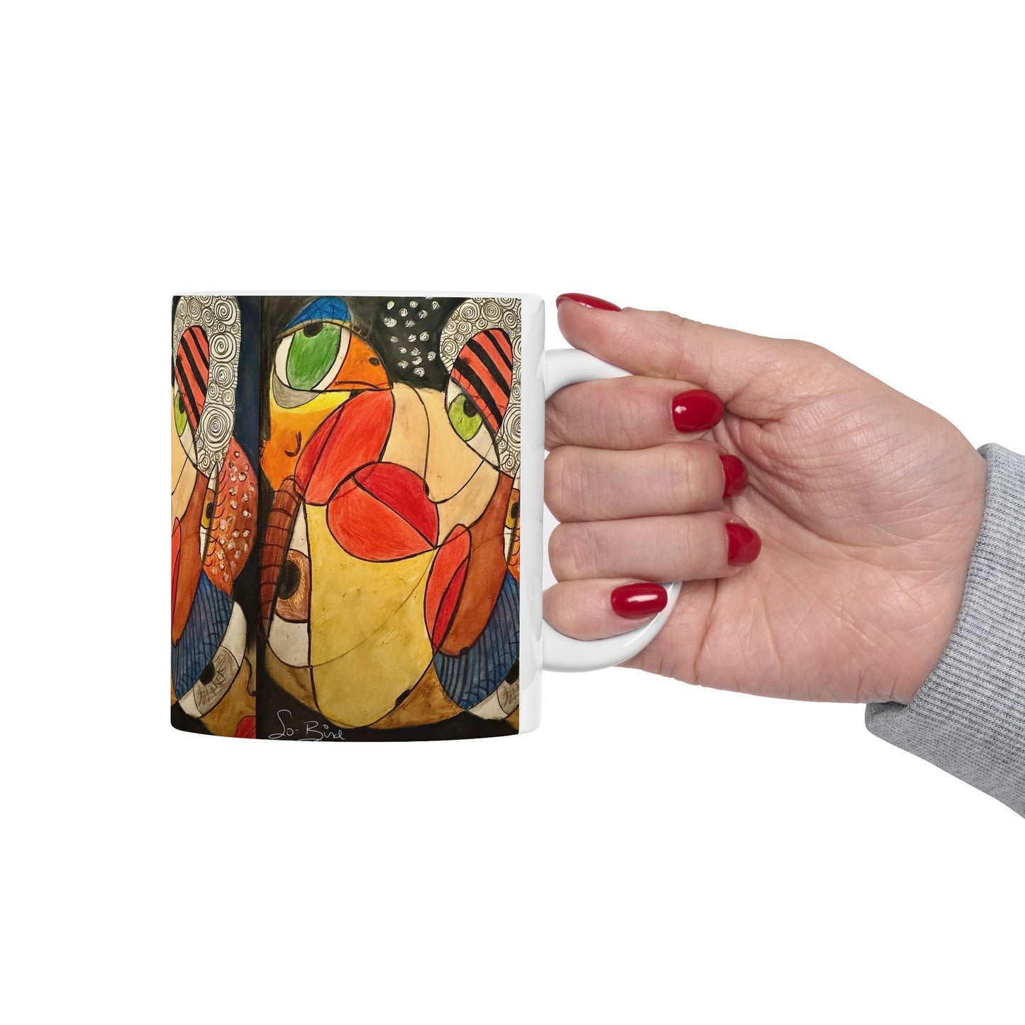 A hand with red nail polish holds the Printify Ceramic Mug - It's a WE thing Recovery and Sober Gift, featuring bold abstract art in red, green, orange, and black. A light gray sleeve is visible—perfect for morning coffee and celebrating sobriety.