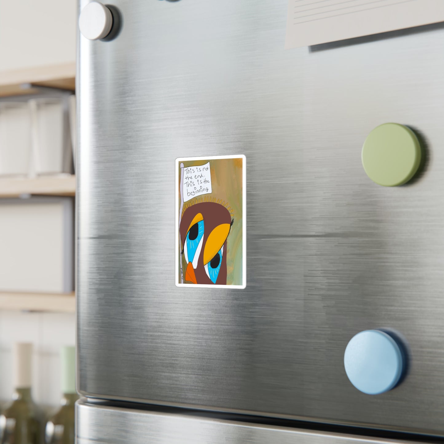 A stainless steel fridge with three round magnets and a "This is Not The End" Vinyl Decal from Printify, a colorful abstract bird design ideal as sobriety gifts. Shelves with jars and containers appear in the background.