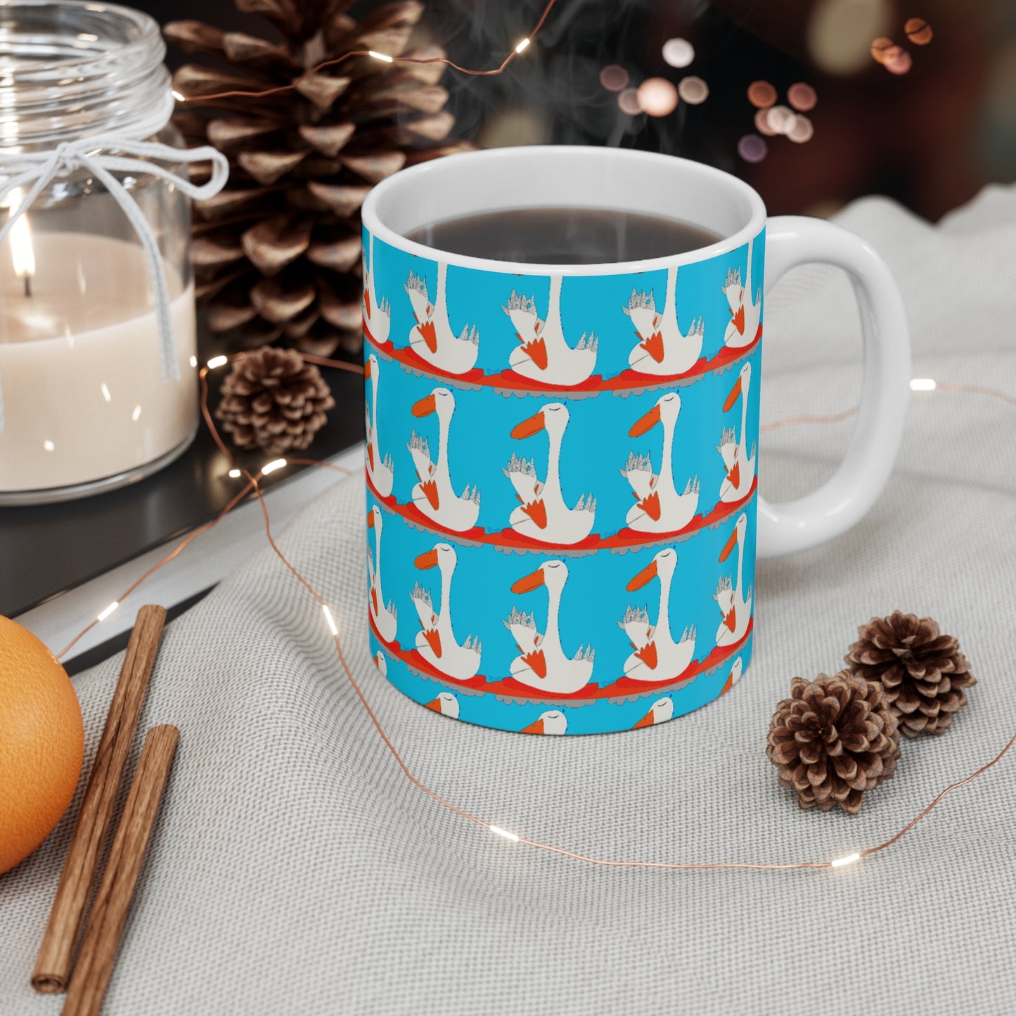 The Many Ducks Mug - 11oz by Printify features a cheerful blue pattern of festive ducks on white. Filled with coffee, it's surrounded by cozy pinecones, cinnamon sticks, orange, candlelight, and string lights—a perfect peaceful sobriety gift.